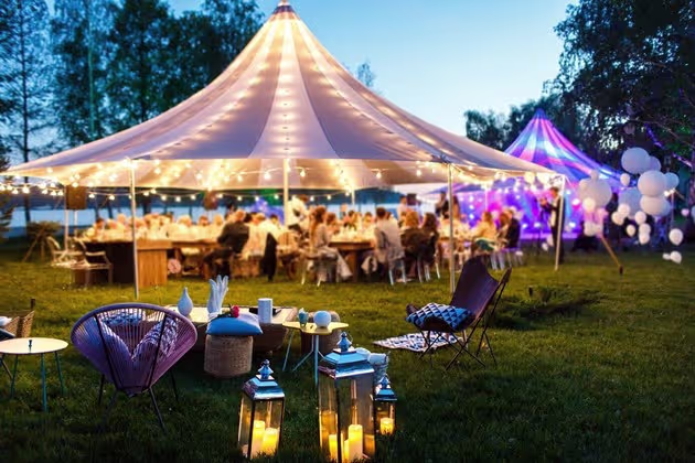 Outdoor wedding reception under a large tent with string lights, lounge seating, and evening ambiance